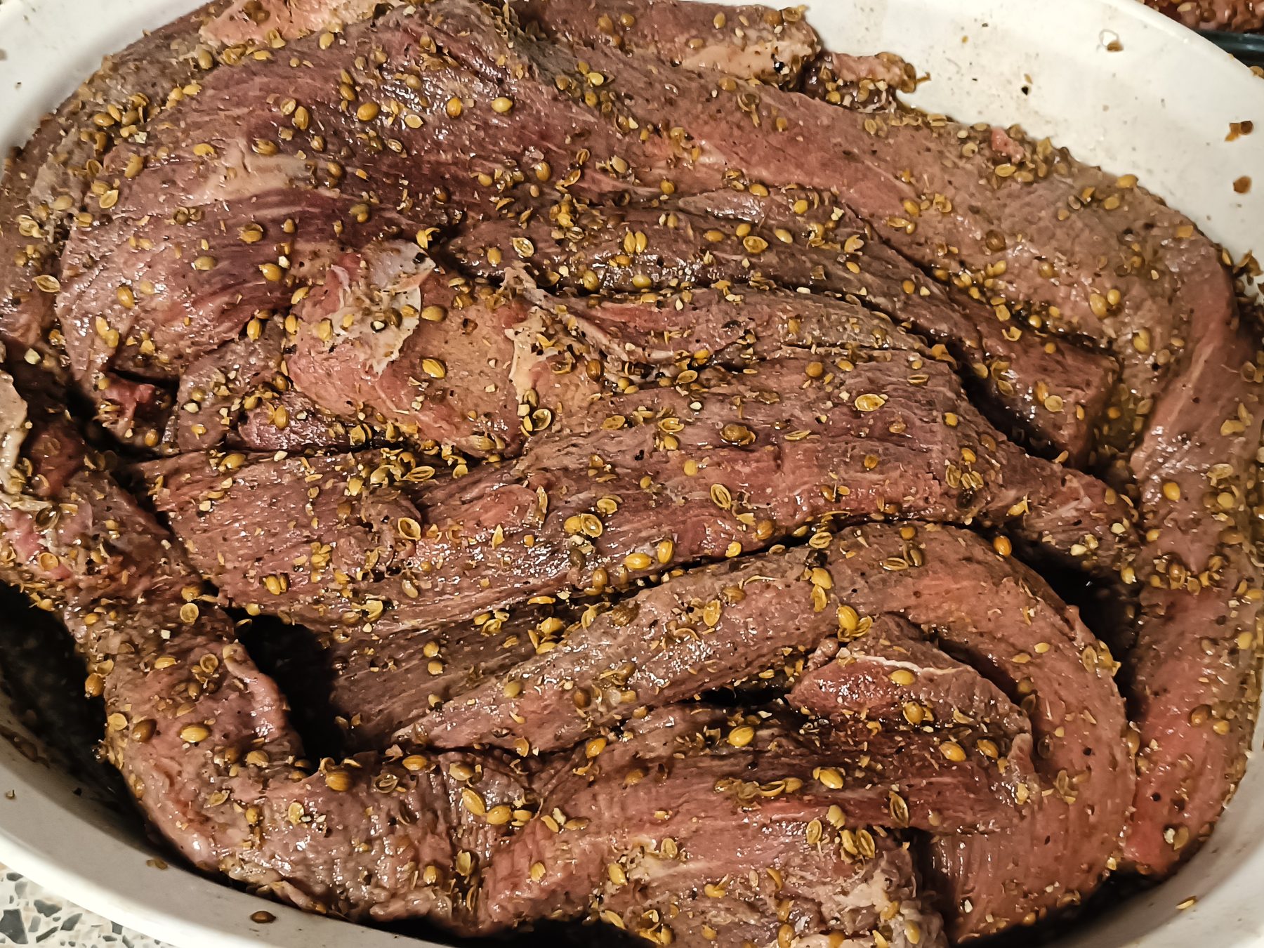 Beef strips coated in whole coriander seeds and cracked pepper, marinating before curing.