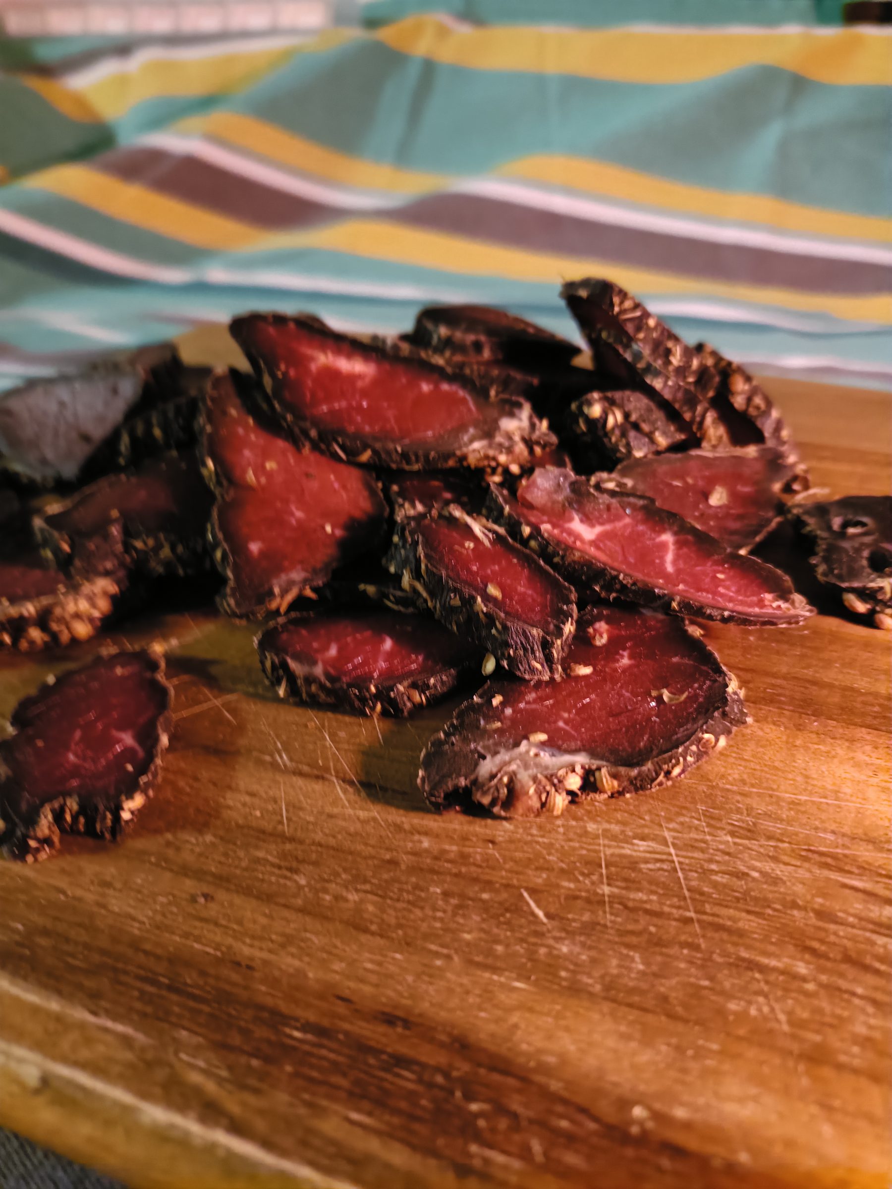 Sliced biltong with a dark spiced crust and deep red centre on a wooden cutting board.