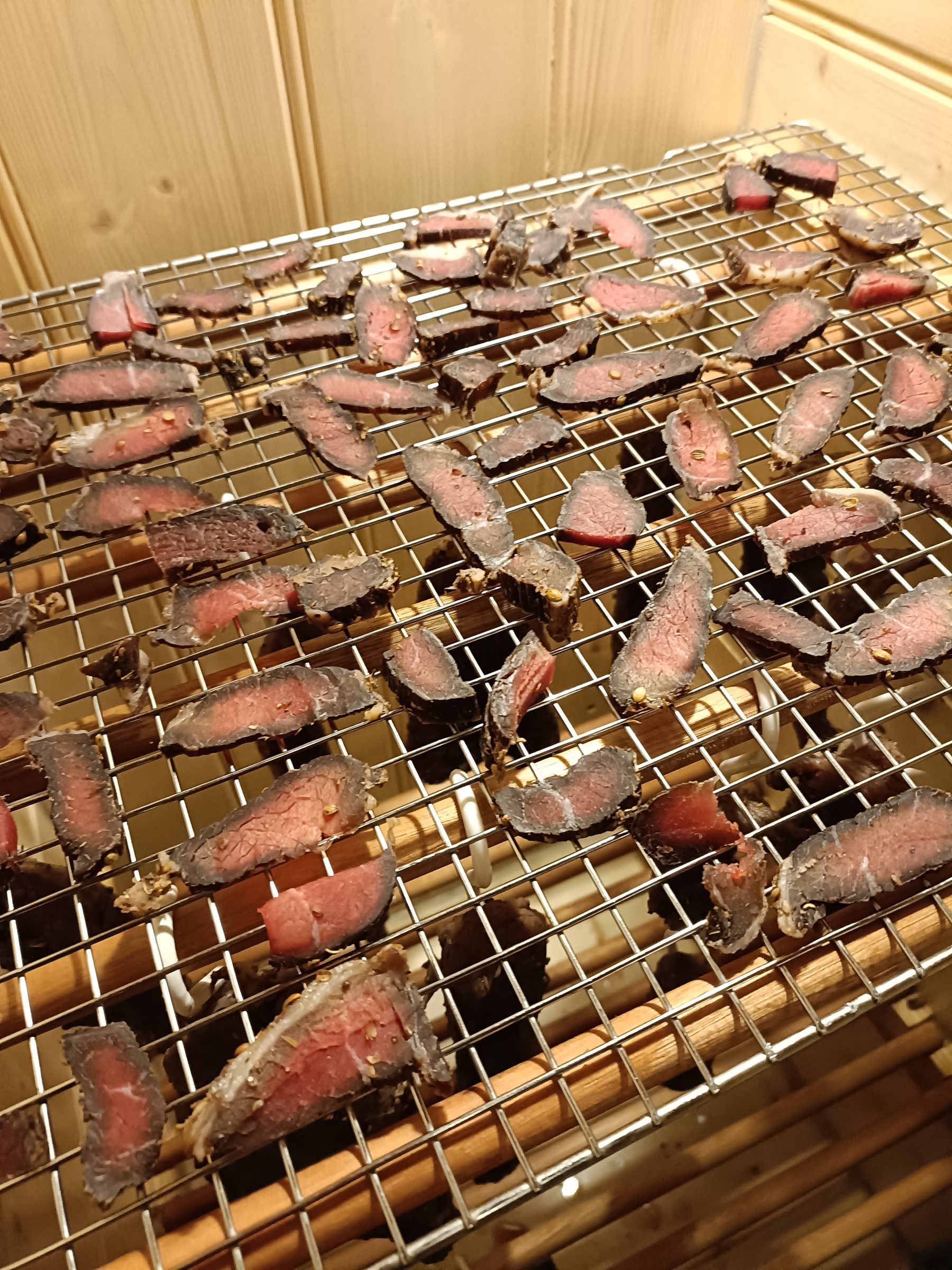 Biltong strips curing on wire racks inside a wooden drying cabinet.